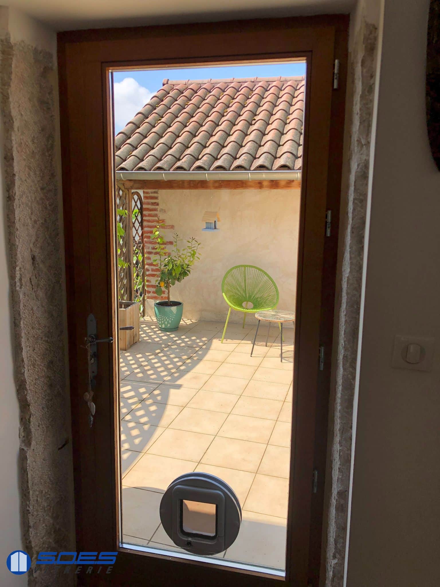 Chatière installée sur une porte vitrée donnant sur une terrasse ensoleillée